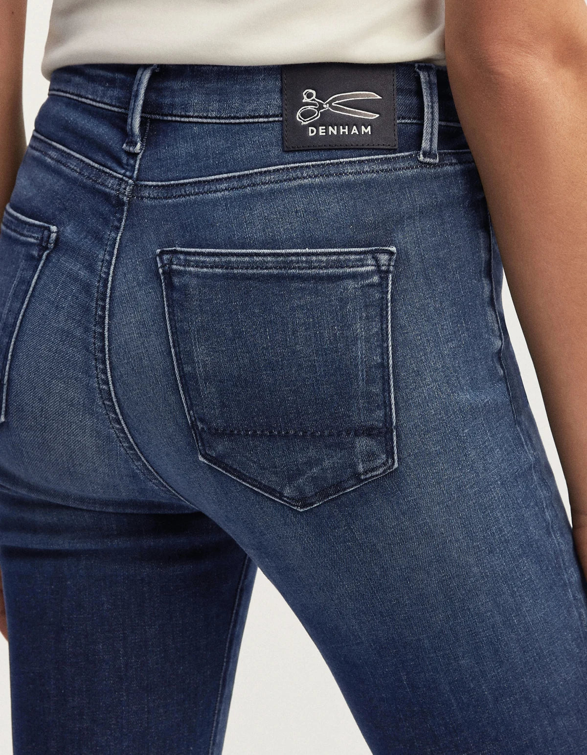 The back view of a woman wearing Denham's NEEDLE Skinny - Dark Soft Wash blue jeans with a 70s vibe.
