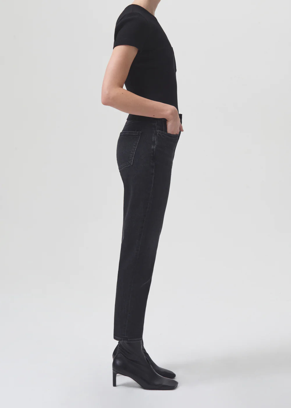 A woman wearing AGOLDE Riley Straight Crop - Panoramic black jeans, a slim straight leg style, and a high-rise black t-shirt.