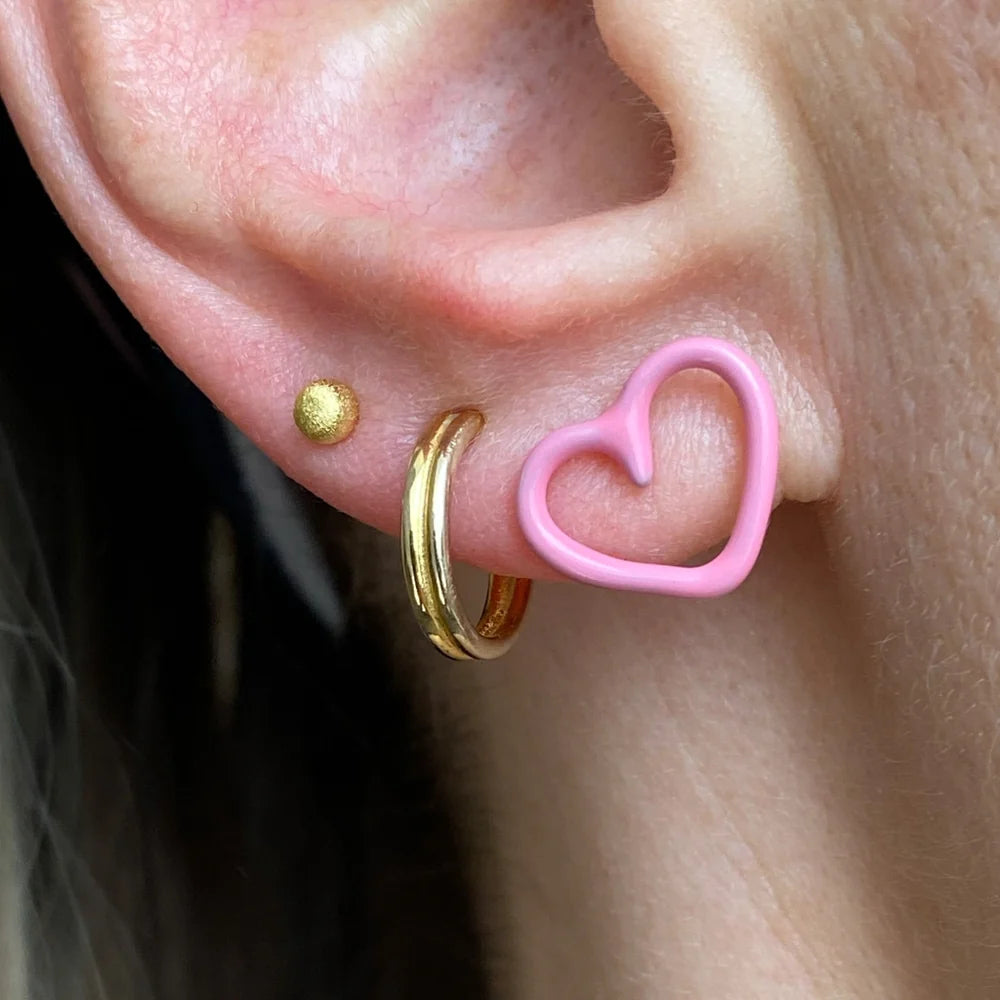 Close-up of a person's ear showcasing three stacking earrings: a Brushed Ball Single Stud - Gold by Lulu Copenhagen, a larger gold hoop, and a pink heart-shaped hoop.