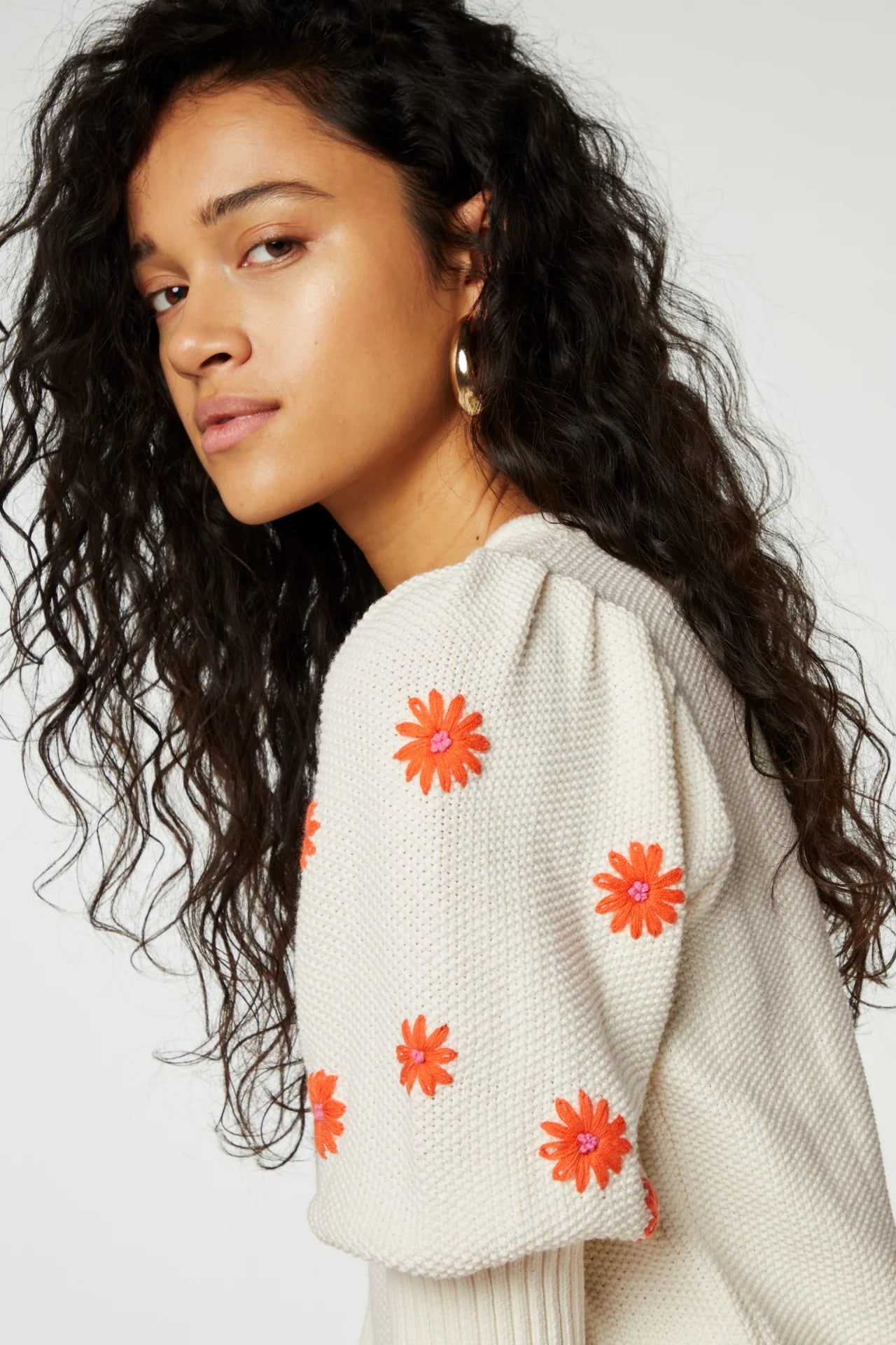 Model wears 3/4 sleeve knit jumper with orange embroidered flowers on sleeves