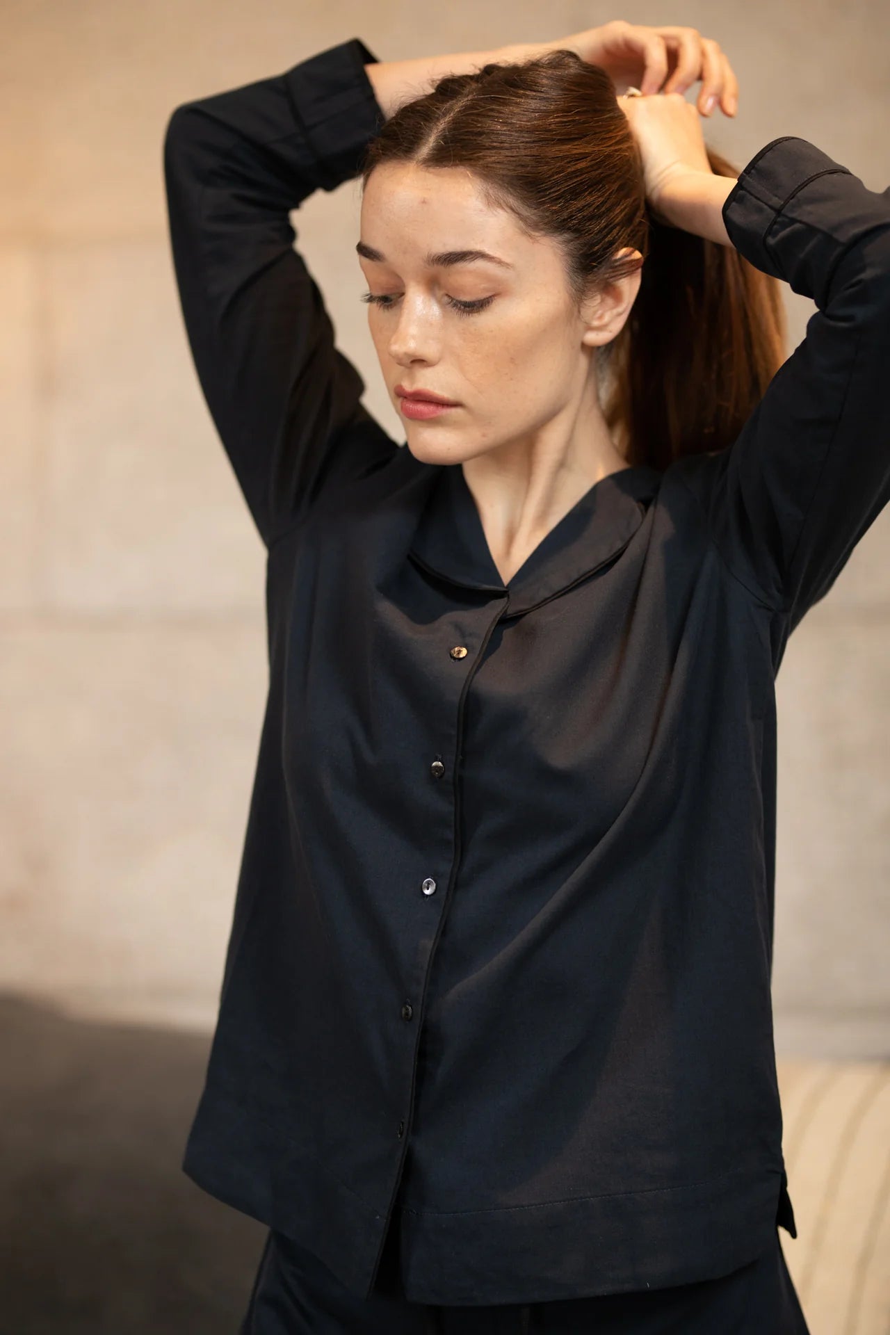 A woman is putting her hair up in a BREATHE Organic Cotton Pyjama Set 'Hang Out' - Navy.
