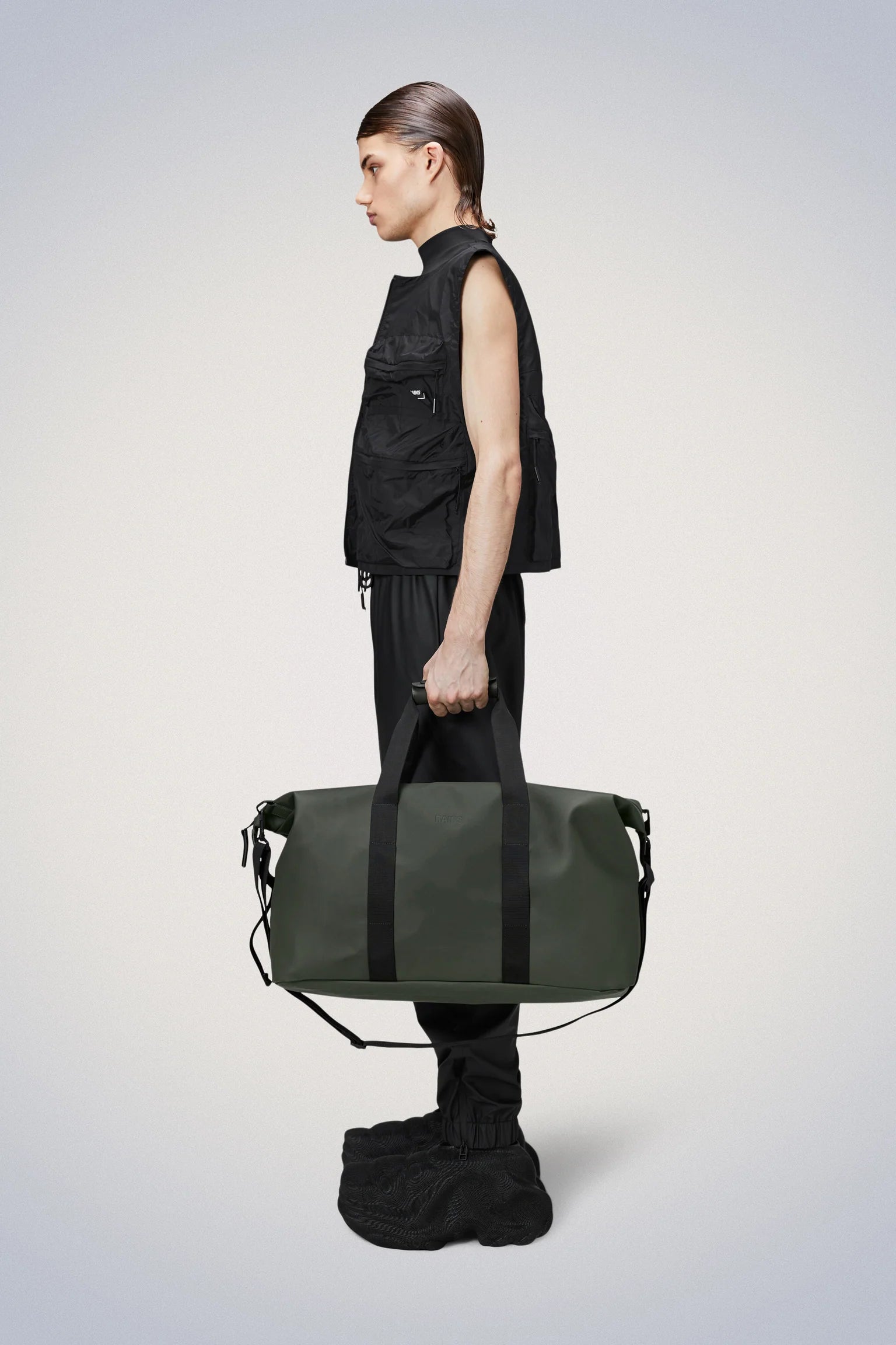 A man is holding his travel-favourite, the Rains Hilo Weekend Bag, a green duffel bag perfect for overnight getaways.