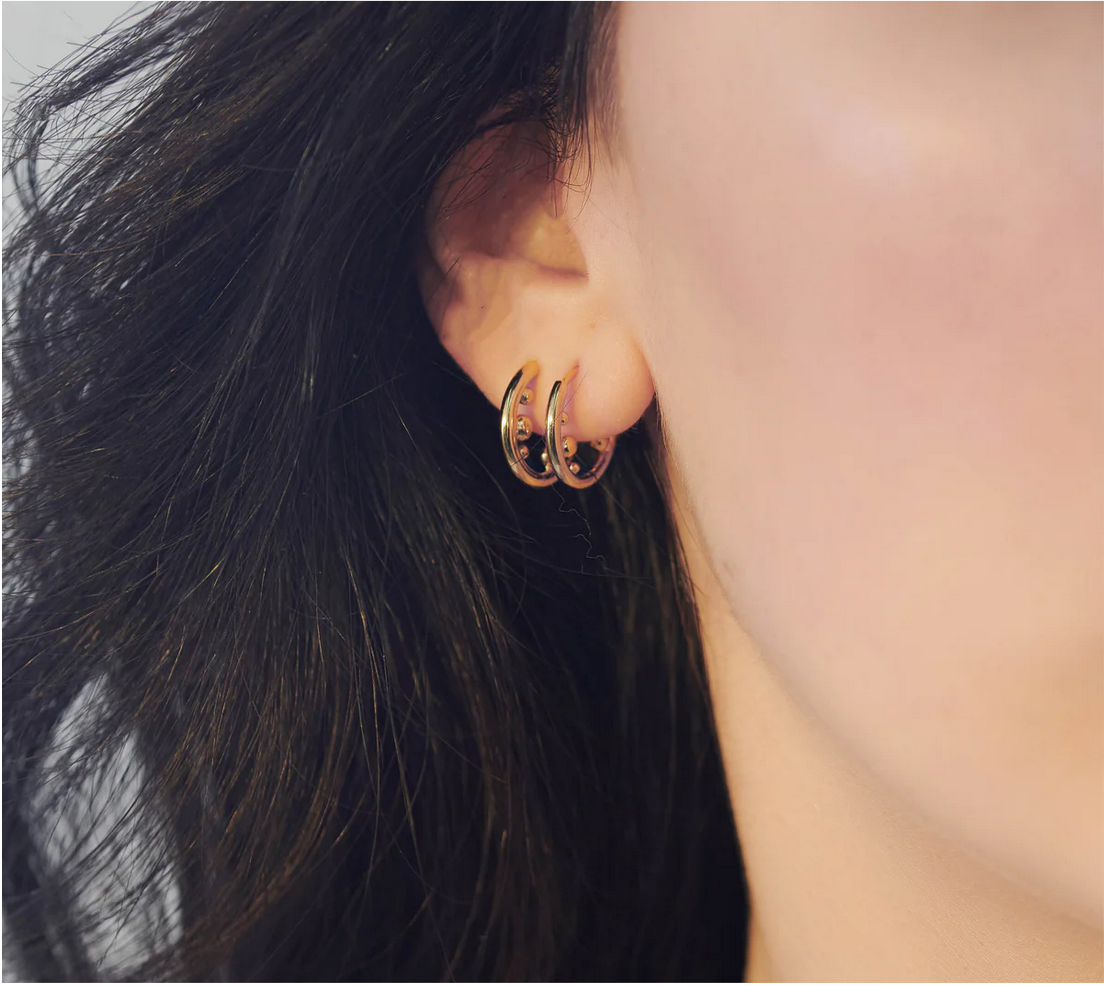 A close up of a woman's ear with Stellar Orb Huggie Hoops - Gold earrings by Rachel Jackson London.