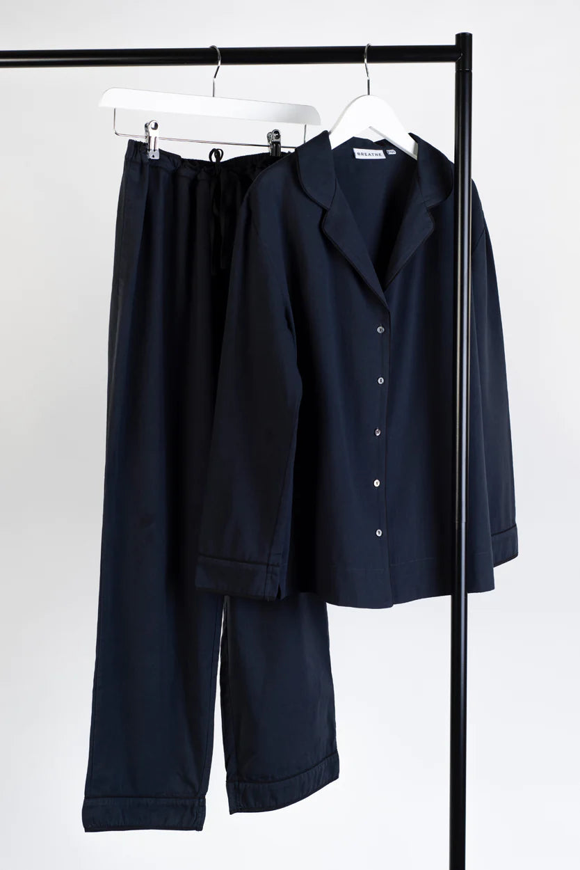 A BREATHE Organic Cotton Pyjama Set 'Hang Out' - Navy consisting of a shirt and pants made from organic cotton, with washing instructions included, hanging on a rack.