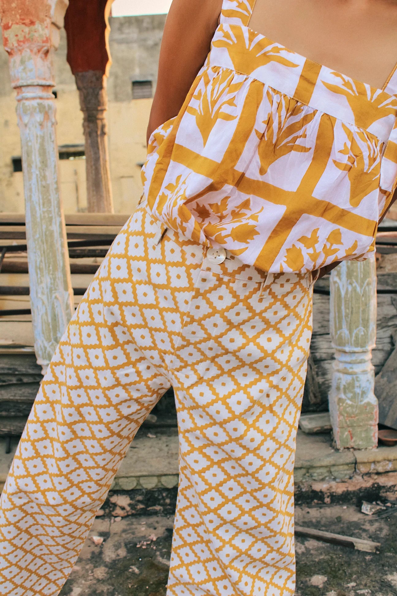 Model wears wide leg cotton trousers with yellow and cream geometric print design.