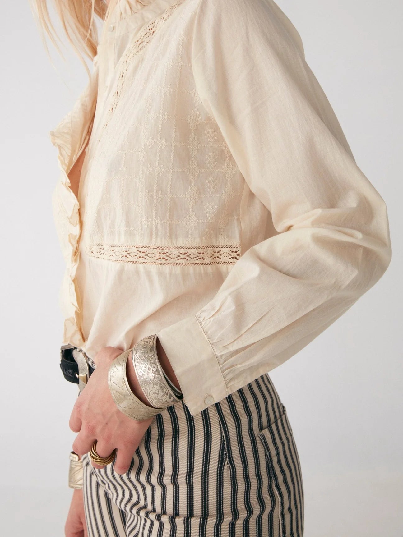 A woman wearing a Riya Blouse - Victorian Ivory by Maison Hotel and striped pants.
