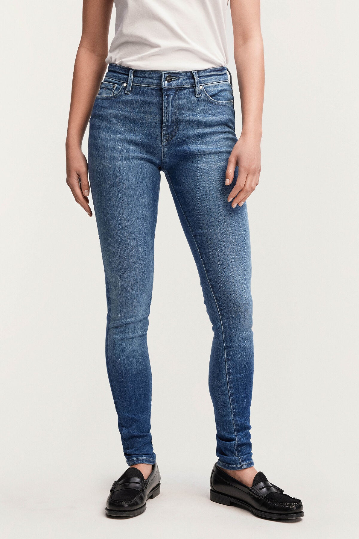 A woman is standing in Denham's NEEDLE Skinny - Light Indigo denim jeans.