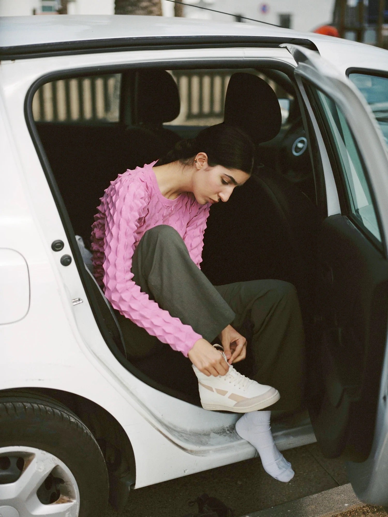 A woman wearing a SAYE Modelo '89 Hi Sneaker sits comfortably in the back seat of a car, enjoying the soft bamboo lining and eco-friendly bio-based vegan leather.