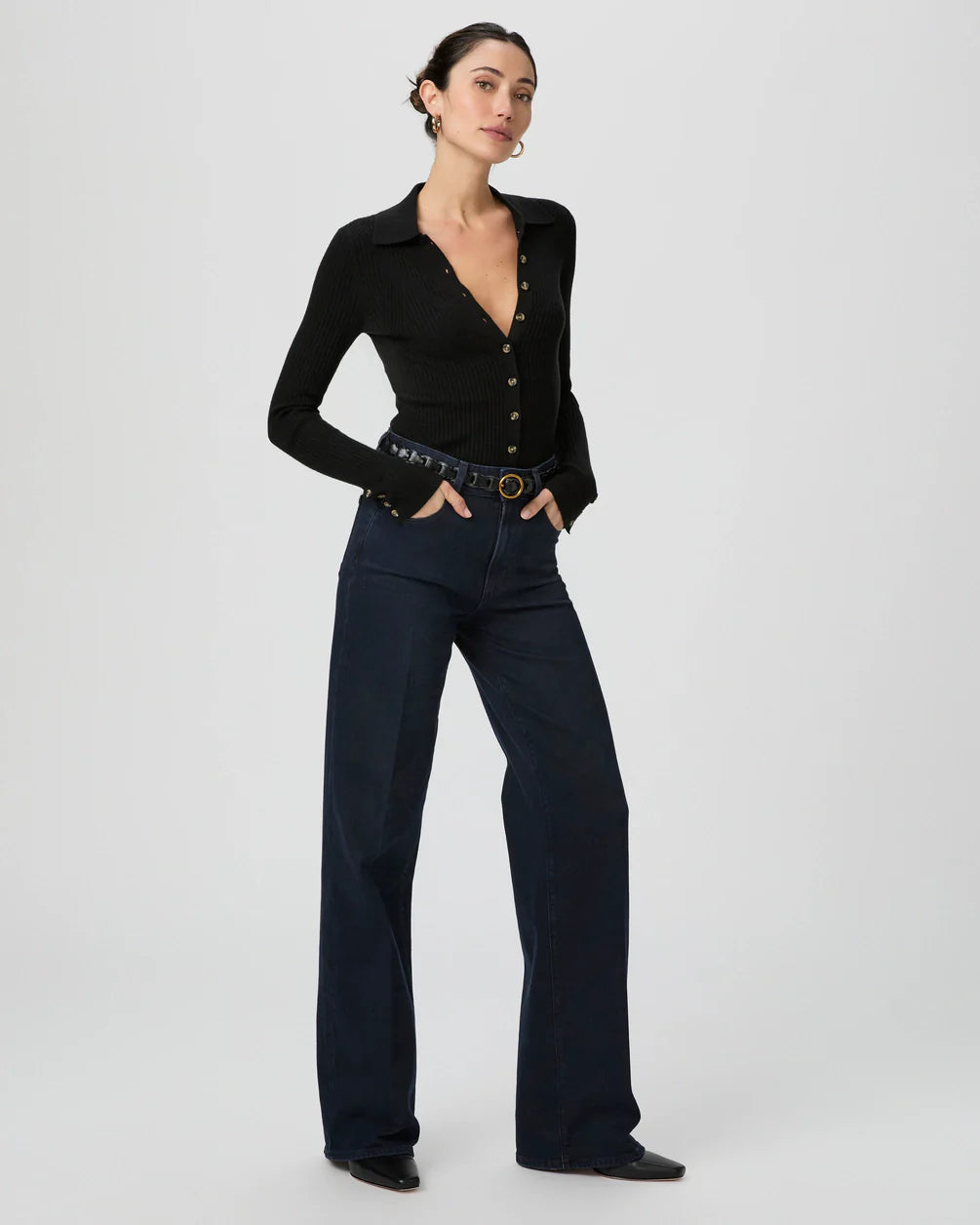 Person wearing navy blue corduroy pants and a black long-sleeve top with their right hand in a back pocket.