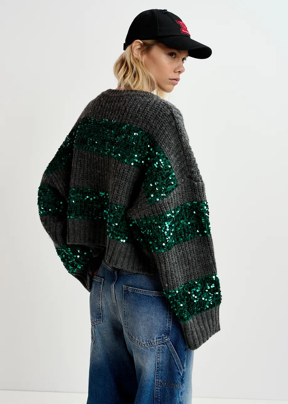 Person wearing a black cap, green and gray sequined sweater, and blue jeans, standing with their back to the camera.