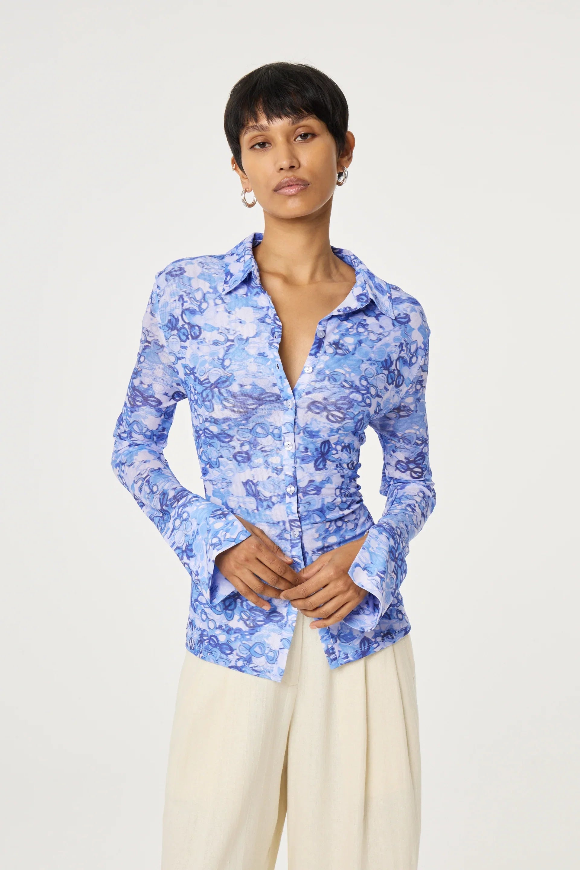 A woman models the Fabienne Chapot Kevis Blouse - Blue, featuring long flared sleeves, paired with cream wide-leg pants against a white background, highlighting a chic and fitted look.
