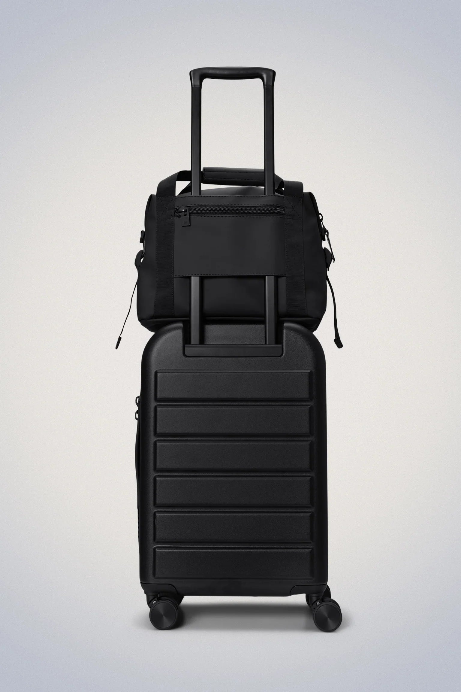 Black wheeled suitcase with an extended handle, topped by a black duffel bag attached securely.