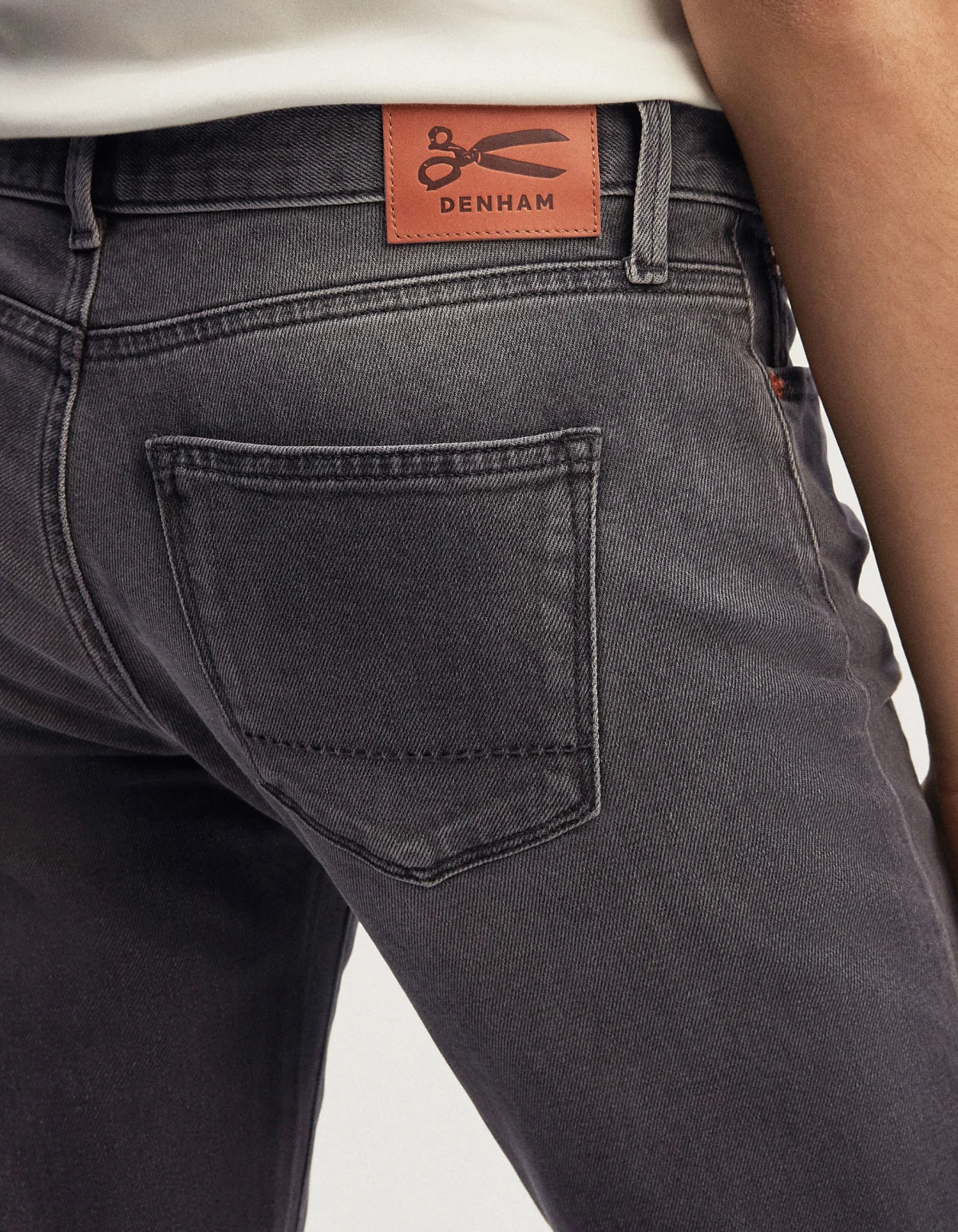The back of a man's mid-rise cut jeans with an orange label, part of Denham's Authentics range in comfort stretch black denim, featuring the MONROE - Authentic Grey Wash.