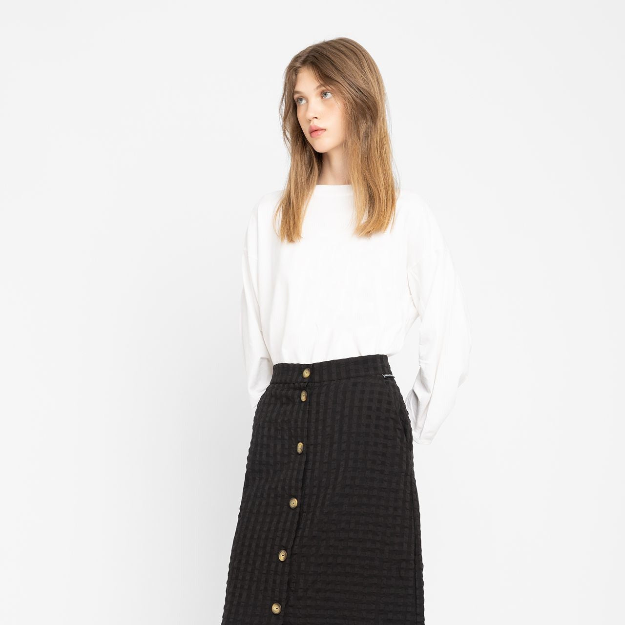 a person wears loreak mendian white structured sleeve t-shirt called Jane with a black skirt on a white background