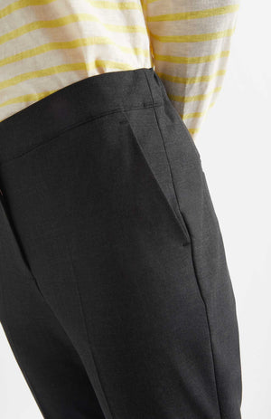Person wears Alaiak trousers in a dark grey shade. The pants are worn with a yellow and white striped long sleeve top. Close up of elasticated waistband.