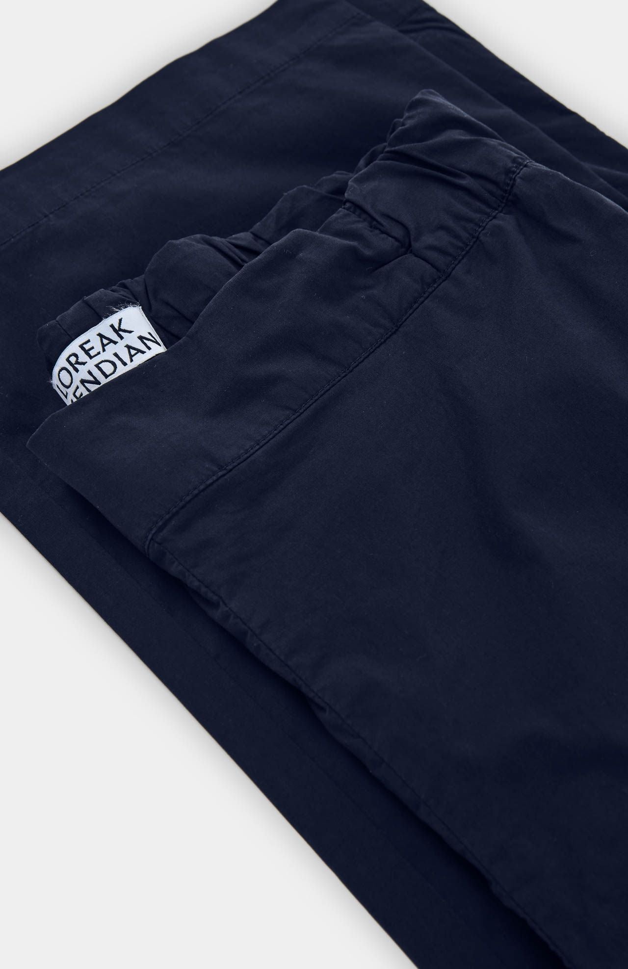 A close-up of Loreak Mendian's Confya Cropped Trousers in navy, featuring a straight-leg cut, elastic waistband, and a partially visible brand label inside.