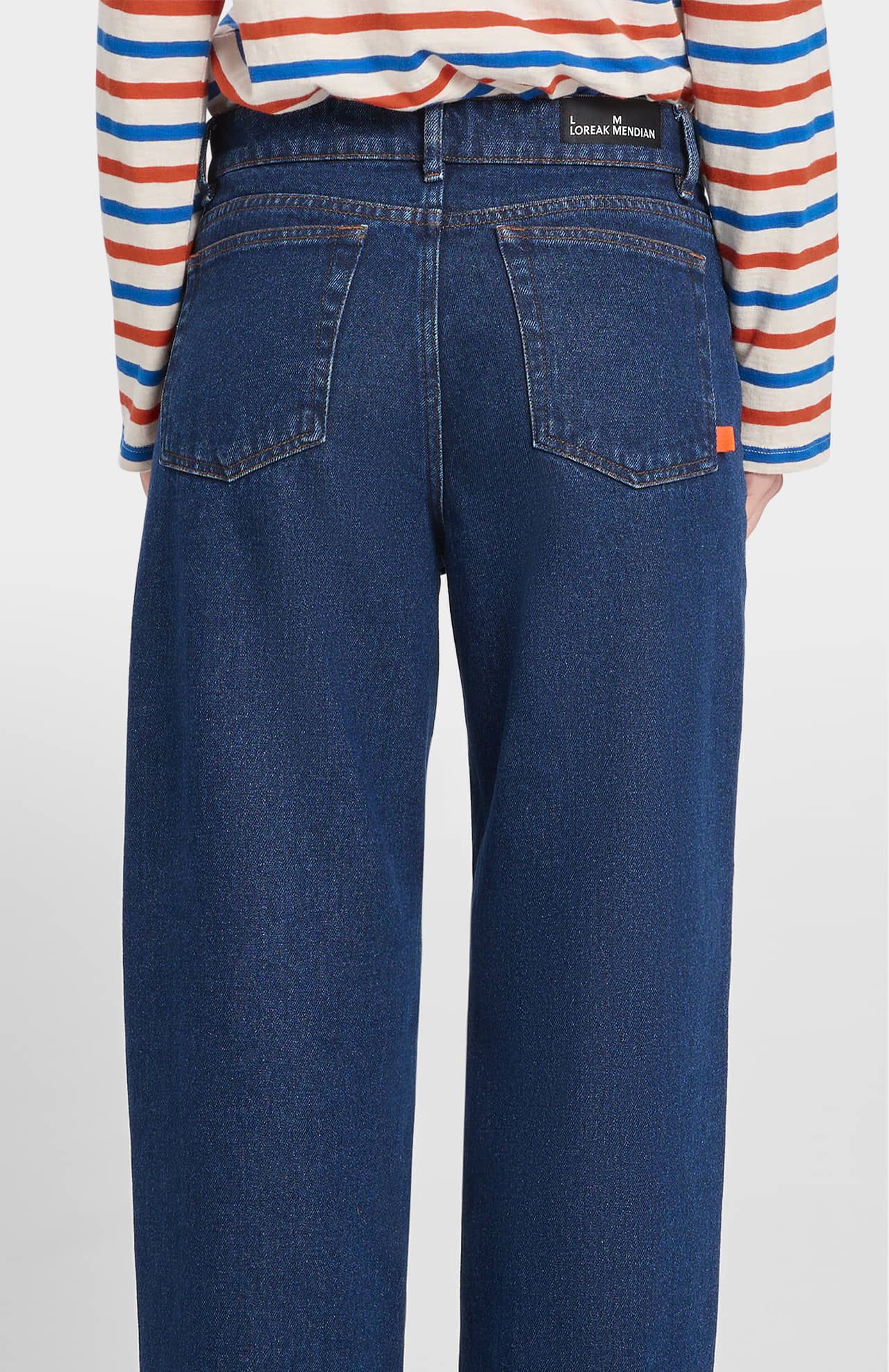 Blue jeans worn by a person with a striped shirt on a white background
