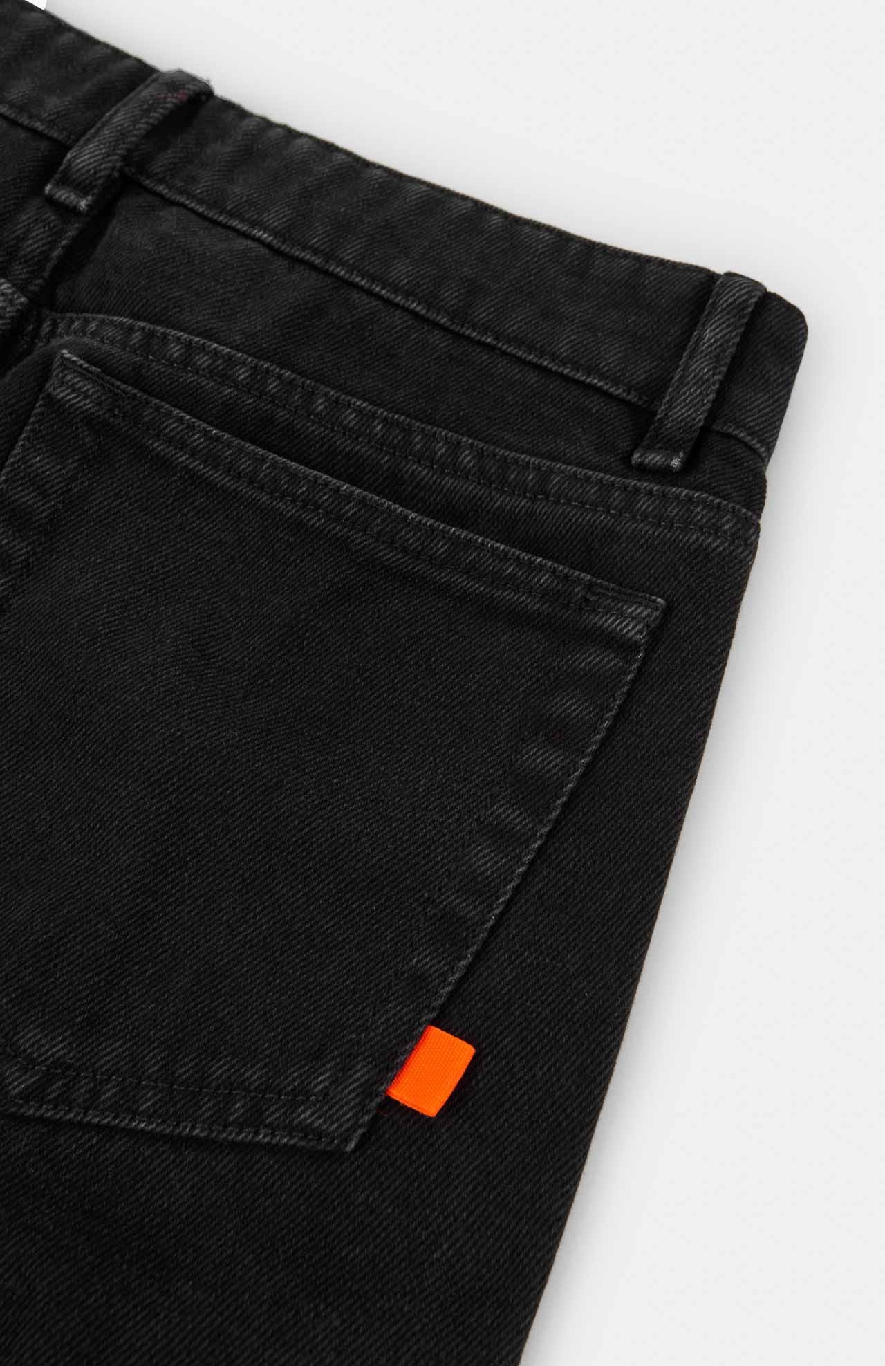 Close-up of Loreak Mendian's Navasota Denim Trousers in black, showcasing a high-waist design with a back pocket adorned by an orange fabric tab. Made from organic cotton, the jeans are displayed in detail against a plain white background.