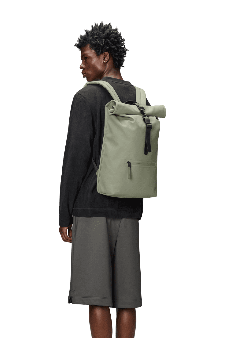 A person in a black sweater and gray shorts is wearing a light green Rains Rolltop Rucksack, facing slightly away. This cycle-ready bag is waterproof and offers ample storage, making it perfect for any adventure.