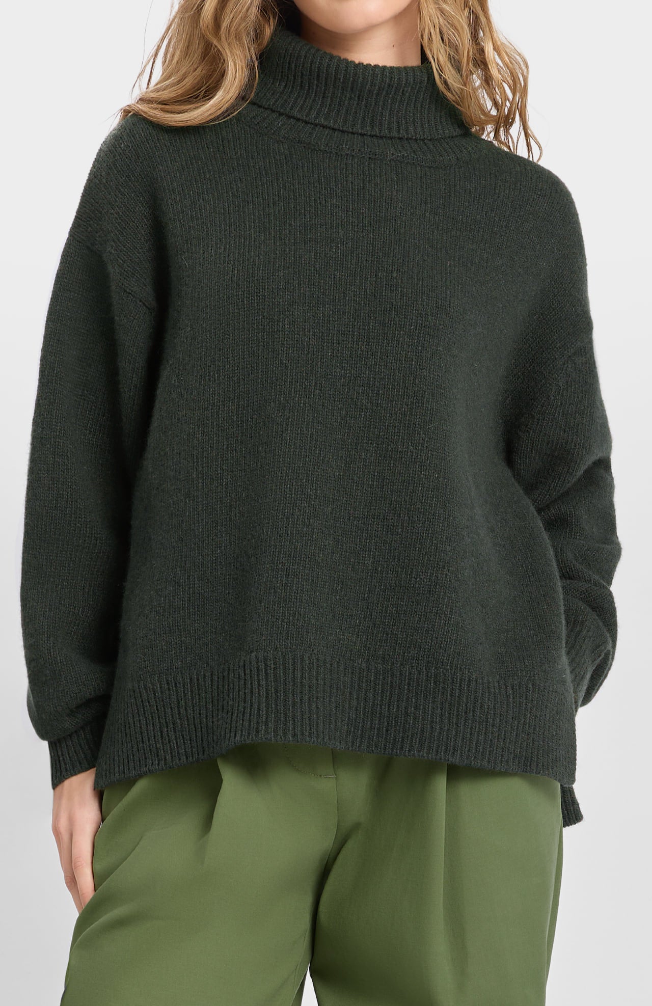Model wears the Loreak Mendian Isla W Jumper in forest green with light green pants, standing against a plain background.