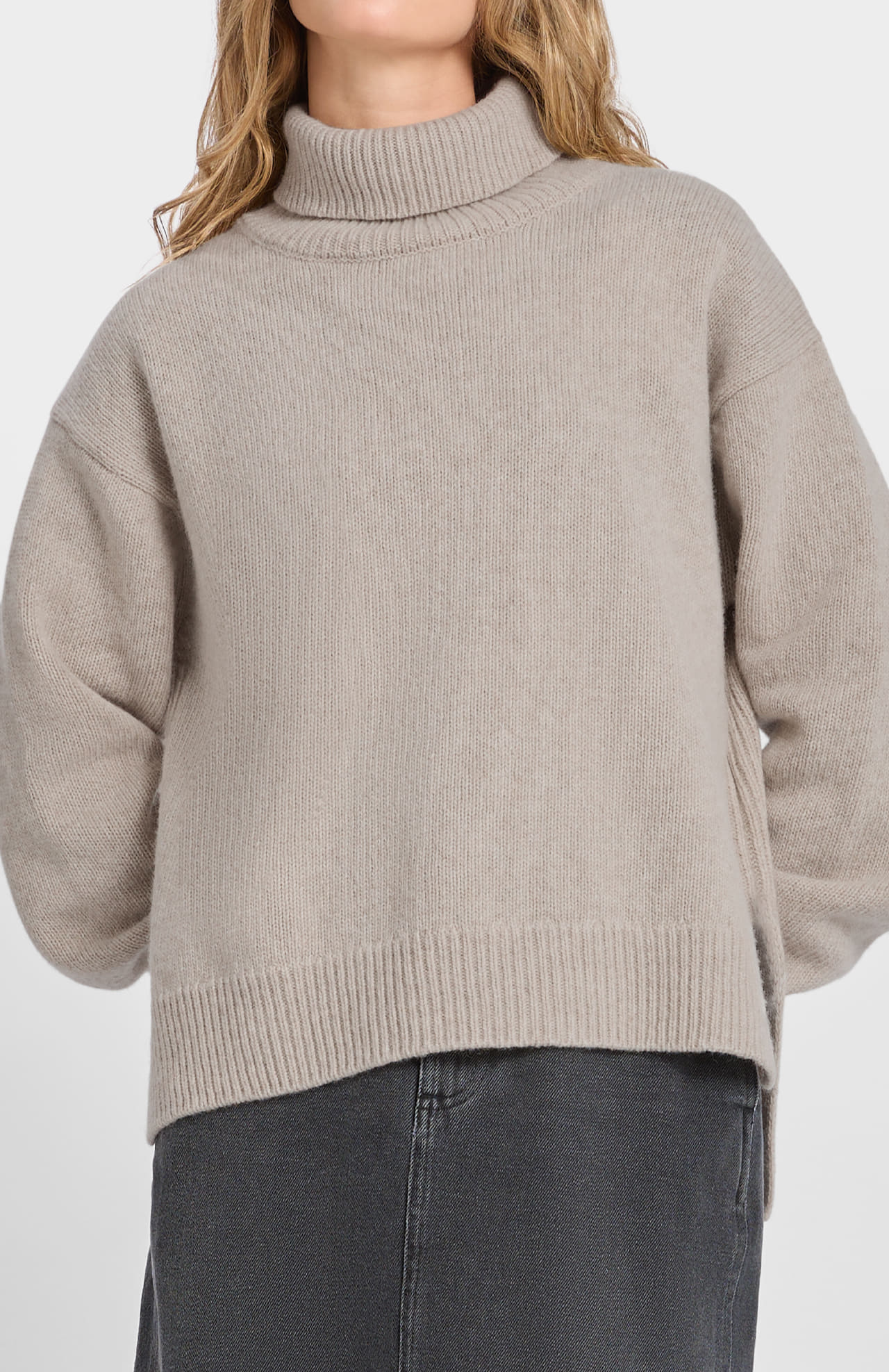 Model wears the Loreak Mendian Isla W jumper in cool beige with a dark gray skirt, shown from mid-chest to knees against a plain background.