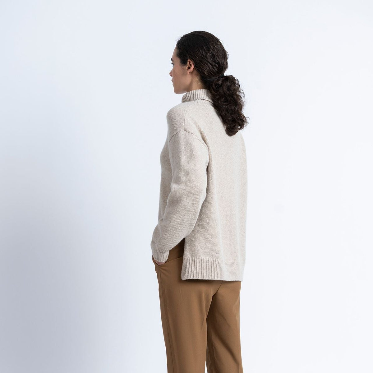 model wears loreak mendian natural colour roll neck knit with camel trousers on a white background.