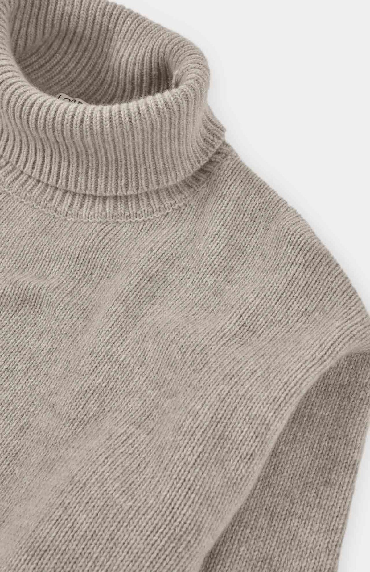 Close-up of a ribbed knit turtleneck sweater in a light taupe-beige color, showing the texture and collar detail against a plain light background.