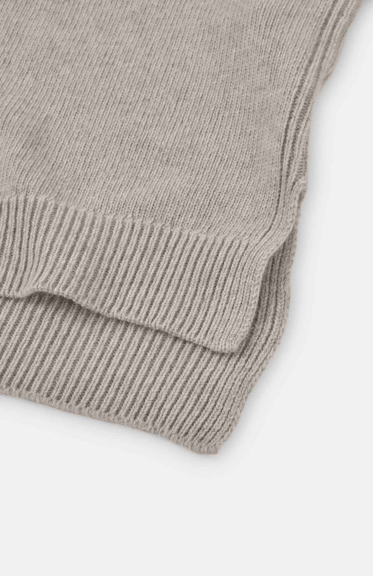 Close-up of the edge of a folded Loreak Mendian Isla W Wool Rollneck Knit in natural, featuring chunky knit ribbed detailing on the hem against a white background.