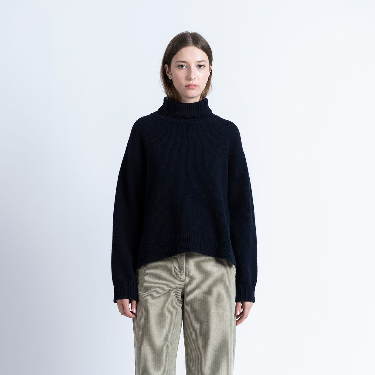 a woman wears navy rollneck knitted sweater with beige coloured cords on a white background