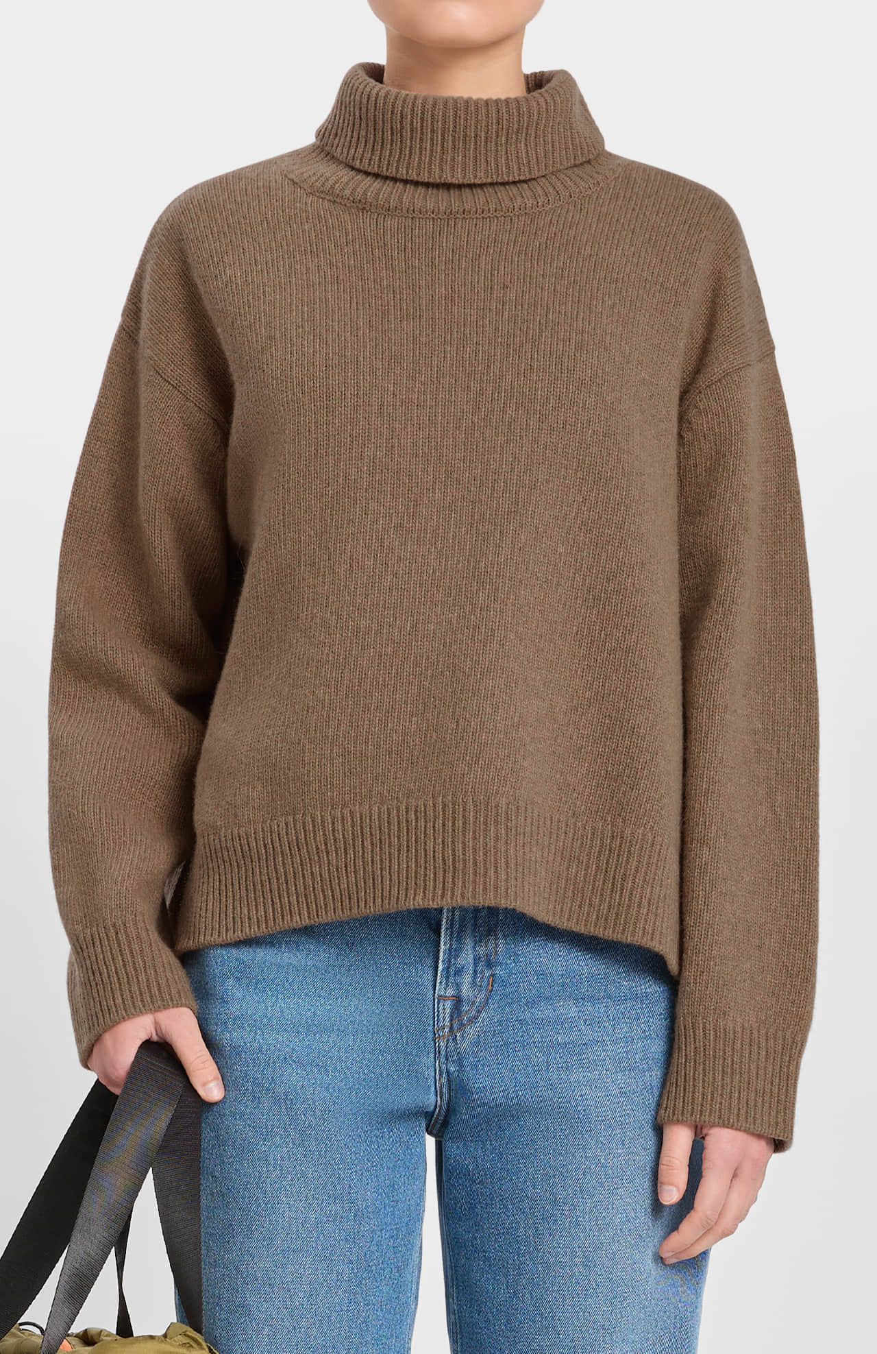 Person wearing a loreak mendian brown sweater and blue jeans on a white background