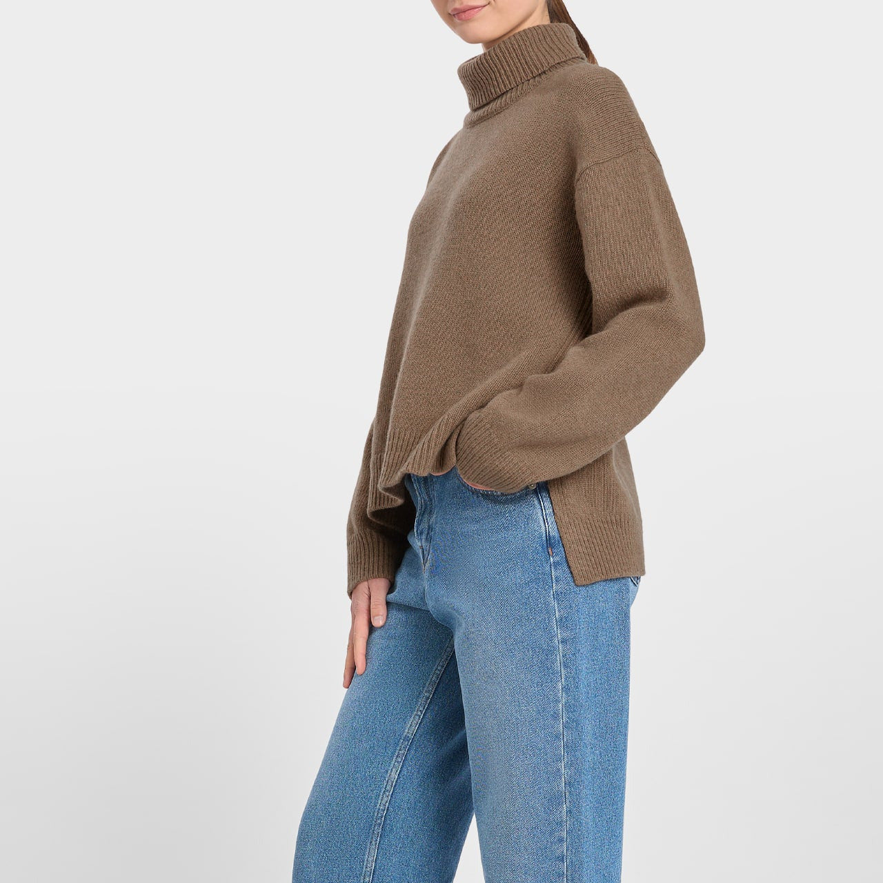 Person wearing a loreak mendian brown sweater and blue jeans on a white background