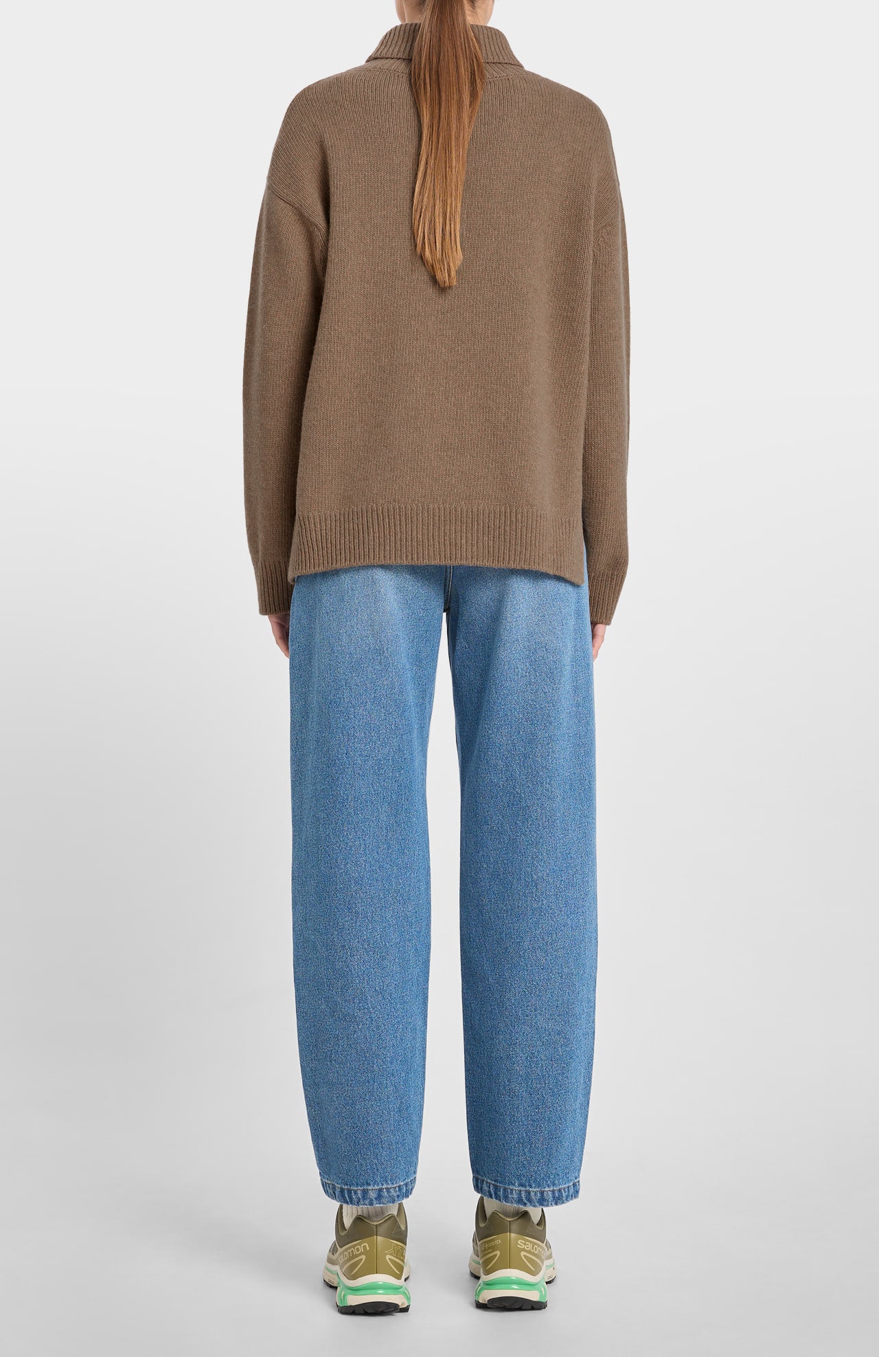 Person wearing a brown sweater and blue jeans on a white background