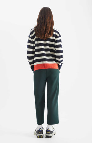Person wears Kada Dot jumper in a navy and white stripe. There is one songle orange stripe at the base and an orange dot at the chest. Back view.