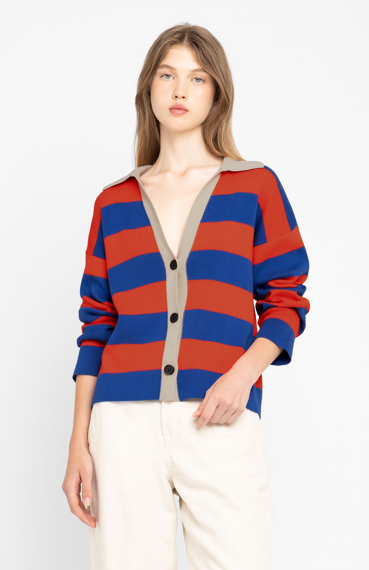 A person wears the Nikole Cardigan - Ink by Loreak Mendian, featuring red and blue stripes, organic cotton material, a classic shirt collar, and beige trim, against a plain background.