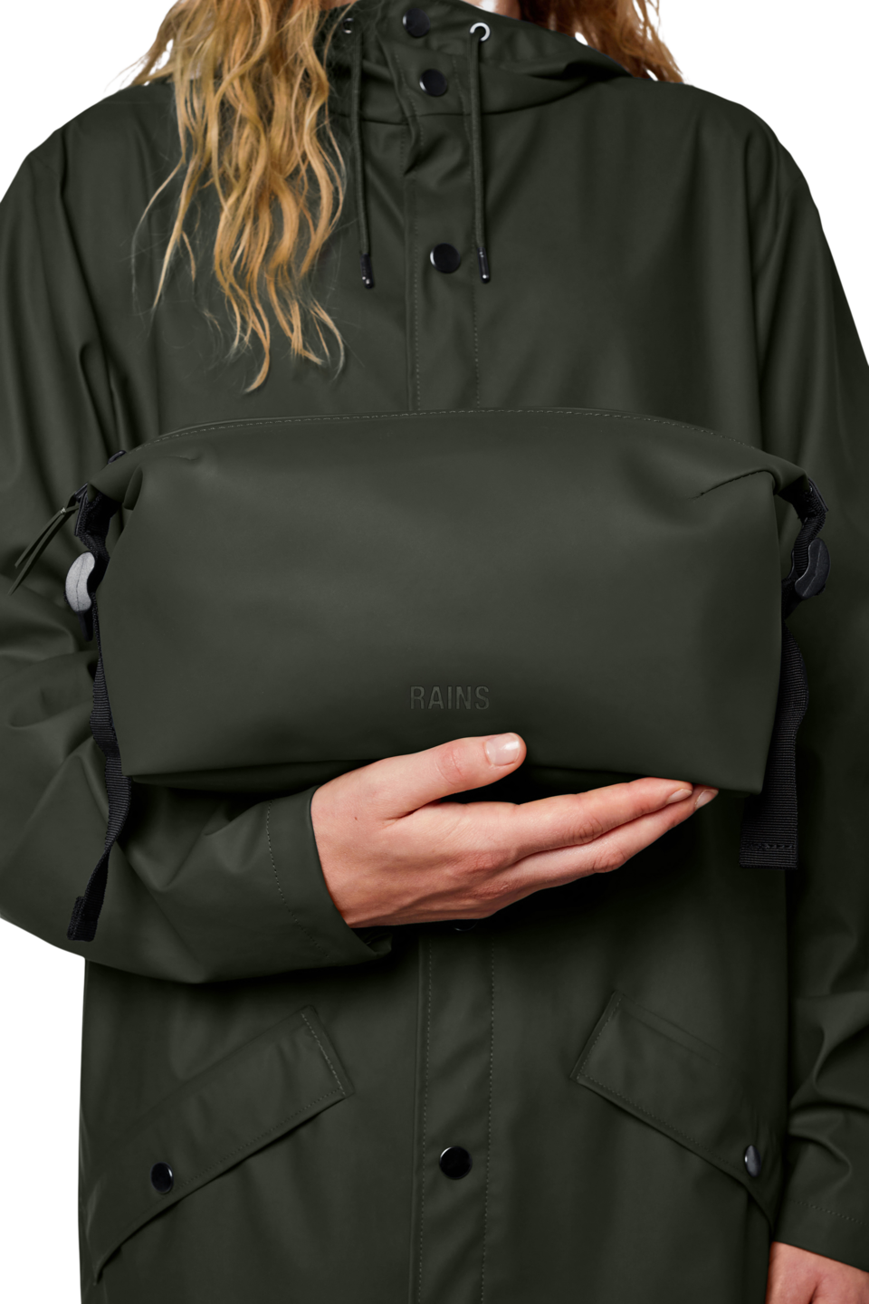 person wearing a green jacket is holding the Green waterproof weekend wash bag by rains - studio shot against a white background