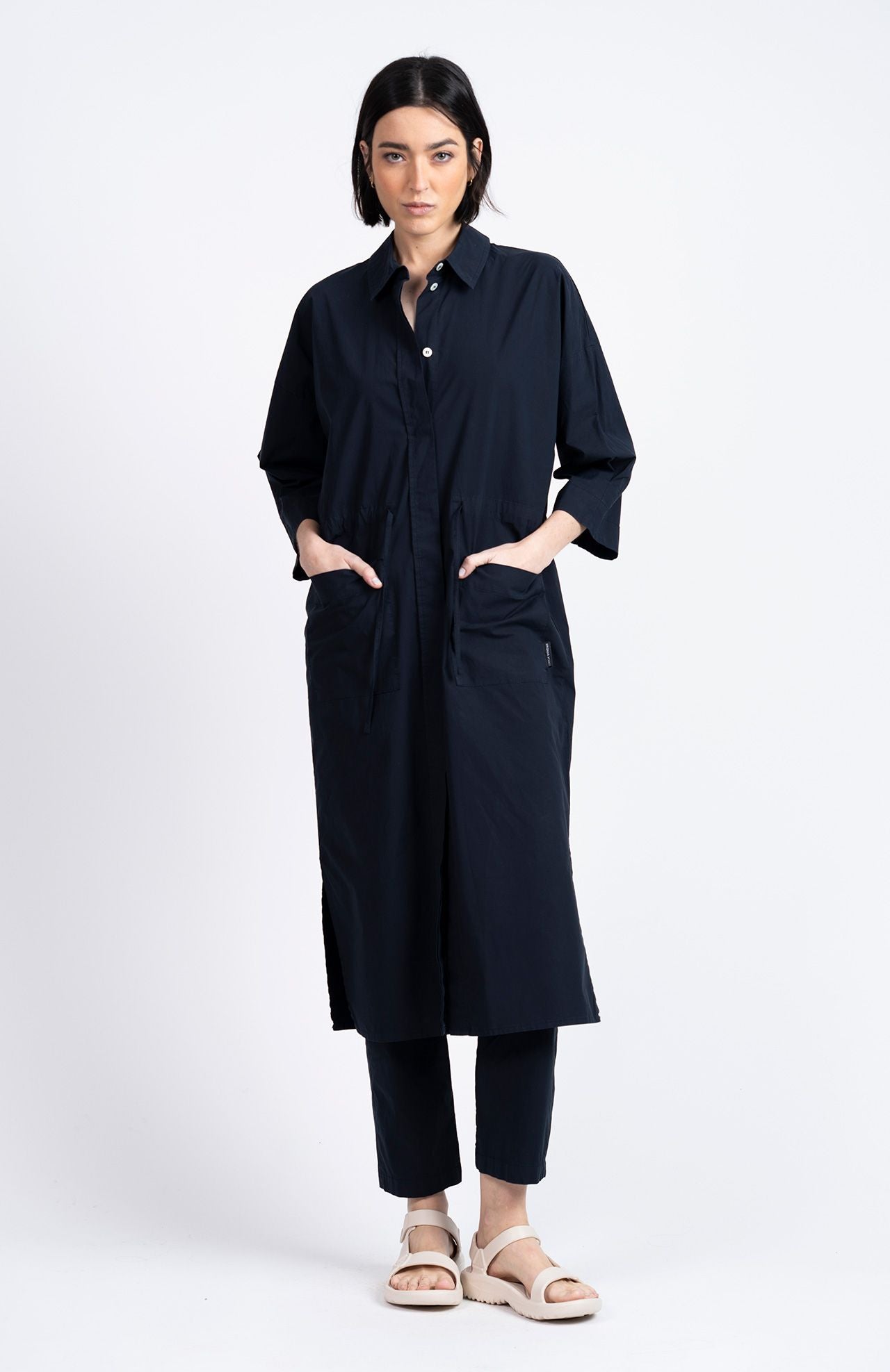 A woman faces forward wearing the Loreak Mendian Lore Dress in navy over matching pants and light sandals, set against a plain white background.