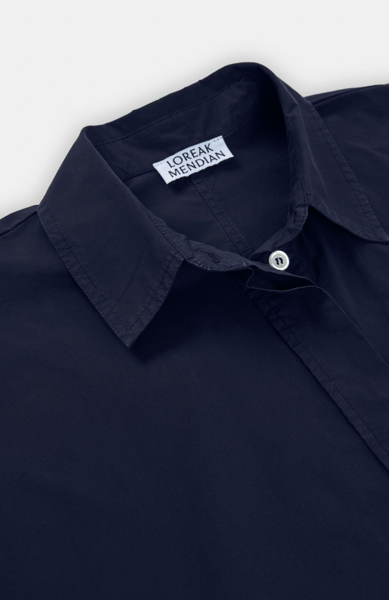 A close-up of the Loreak Mendian Lore Dress in navy poplin, showing a white button and the "Loreak Mendian" label inside the collar.