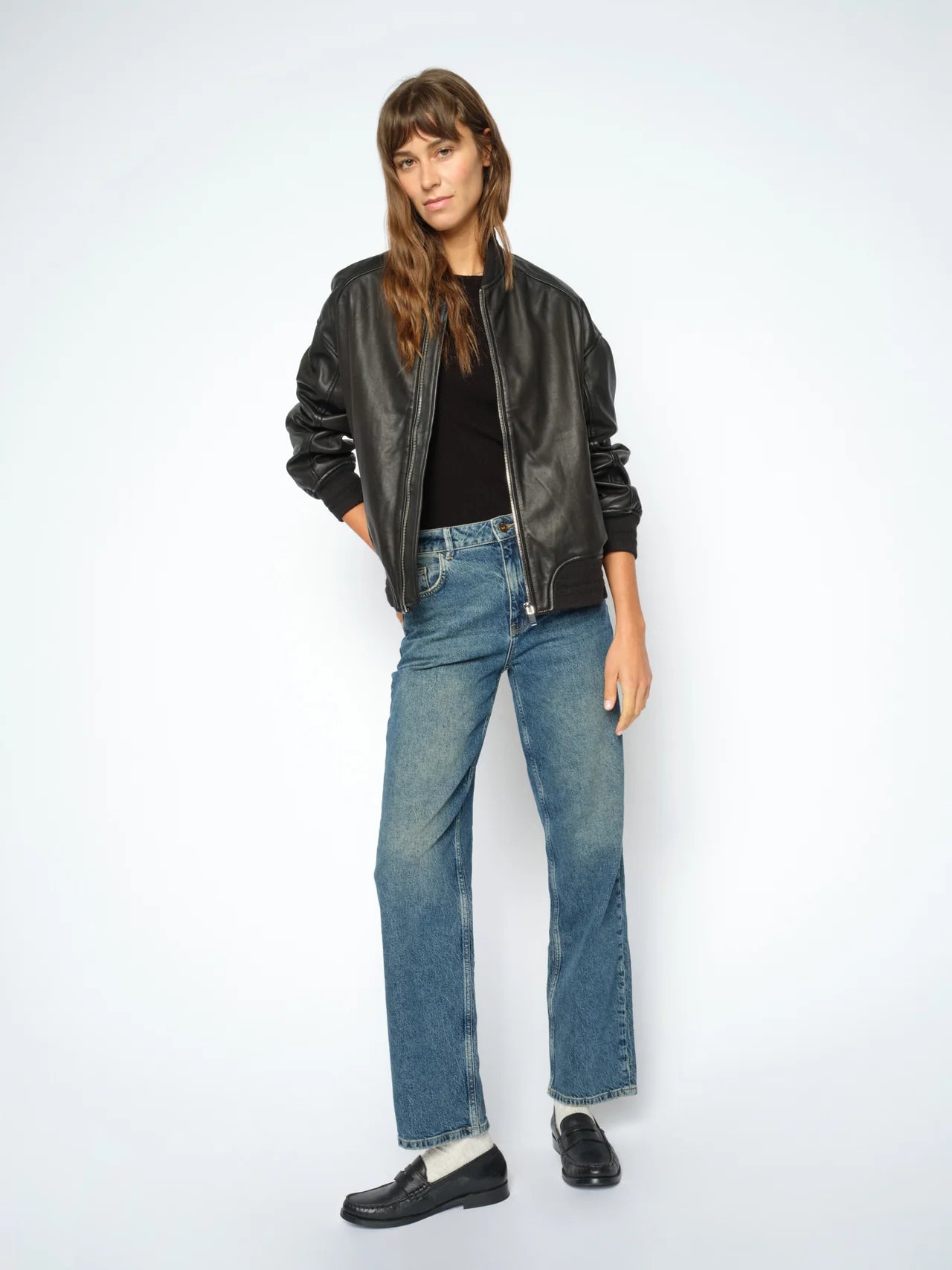 Woman wearing a black leather jacket, black top, and blue jeans on a white background