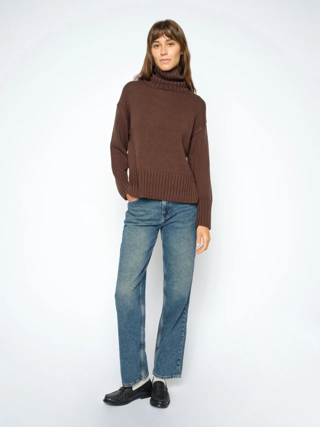Person wearing a brown sweater and blue jeans on a white background