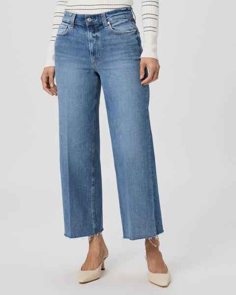 A person wearing the Paige Anessa Wide Leg - Poet jeans with frayed hems and a white sweater with striped sleeves, adding a vintage denim flair.