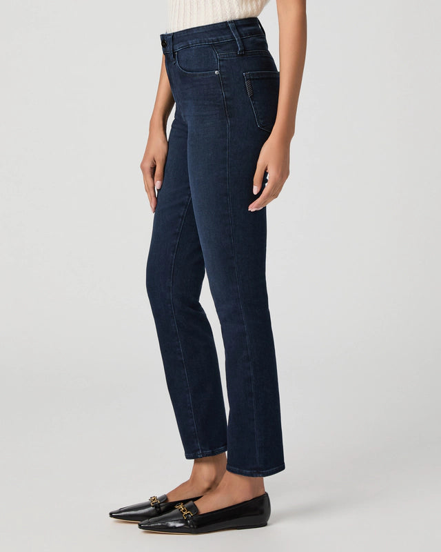 A person wearing Paige Gemma Cigarette Leg - Bespoke jeans, a light-colored sleeveless top, and black loafers stands against a plain light background.