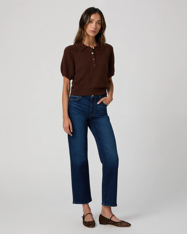 A woman stands against a plain background wearing a brown short-sleeve polo, Paige Mason Ankle Straight - Overdrive mid-rise straight leg jeans, and leopard print flats.