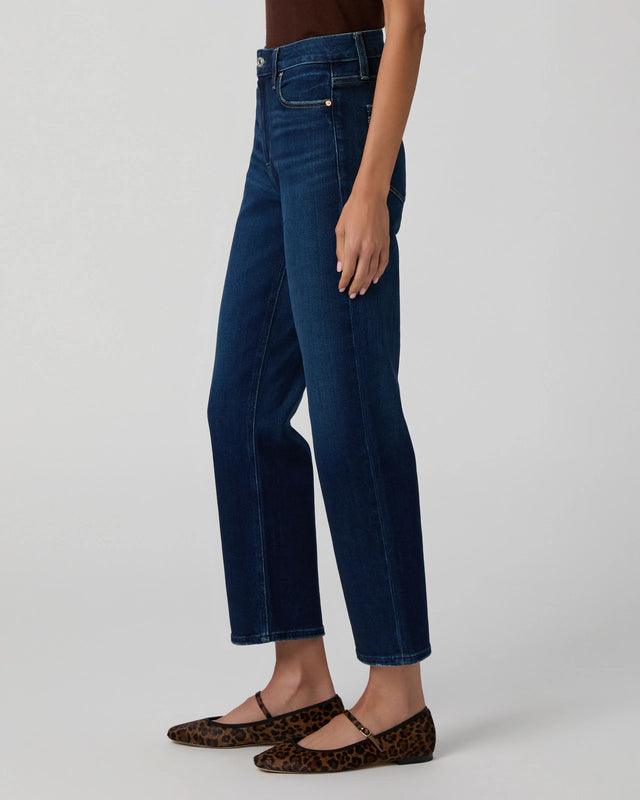 Person wearing Mason Ankle Straight - Overdrive jeans by Paige in dark blue, paired with leopard print flats and standing against a plain light background.