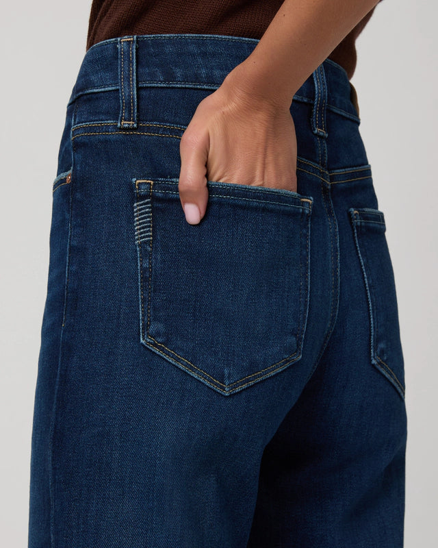 Someone wearing the Paige Mason Ankle Straight jeans in Overdrive denim and a brown top places their hand in the back pocket of the jeans.