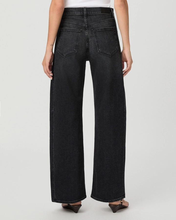 A person is shown from the back wearing the Paige Arellia Skimmer Barrel Leg - Oscura jeans, featuring a high-rise, barrel-leg silhouette in a vintage black wash, paired with a white top and set against a plain light background. The relaxed fit of these Heritage denim jeans is emphasized in the look.