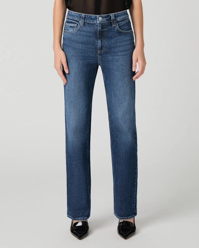 A person wearing Paige’s Stevie High Rise Straight Leg - Jetty jeans in a heritage-inspired medium-blue wash with black pointed-toe shoes, shown from the waist down against a plain light background.