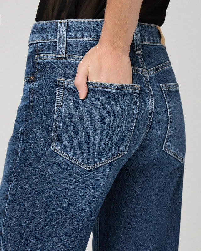 A person is shown from the waist down against a plain background, wearing the Paige Stevie High Rise Straight Leg - Jetty jeans in a medium-blue wash, with one hand placed in the back pocket.