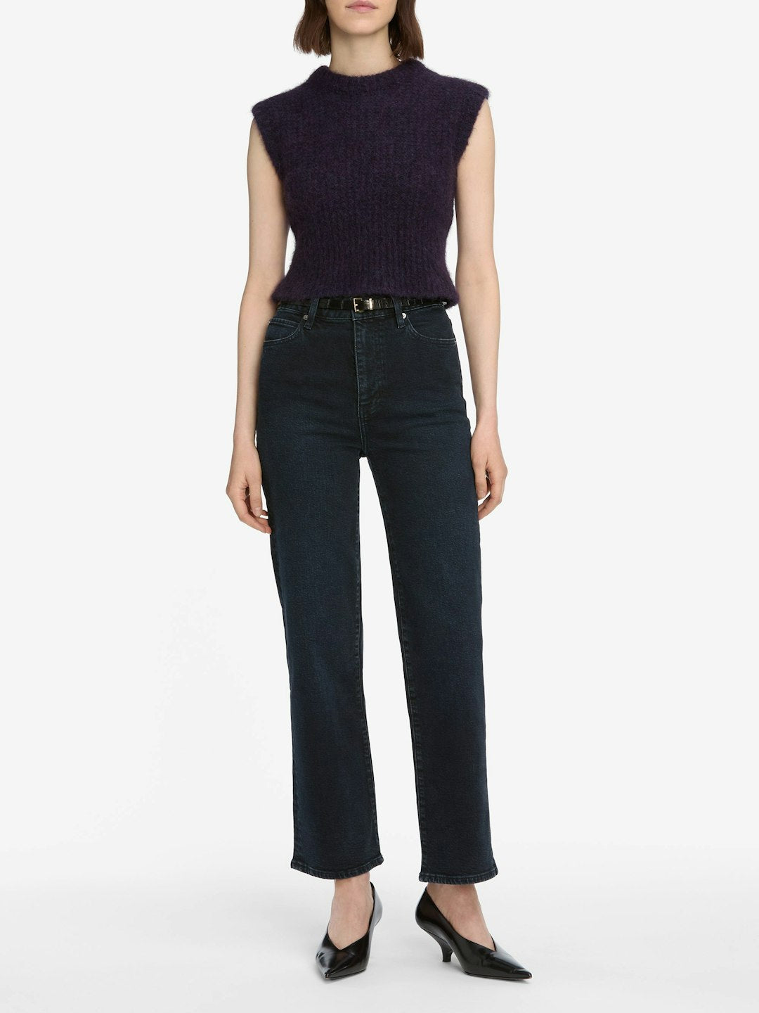 A person in a sleeveless dark purple knit top, Frame The Wide - Untold ultra high-rise wide leg dark navy indigo wash jeans by Frame, and black heeled shoes stands against a plain white background.