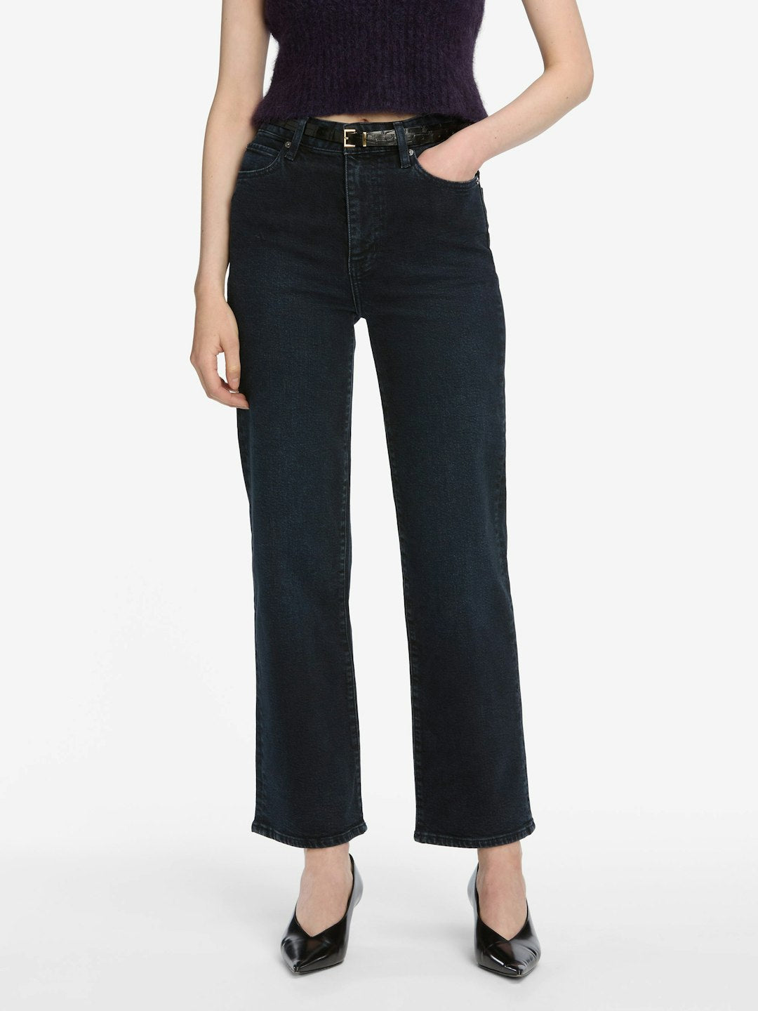 Wearing Frame The Wide - Untold jeans from Frame, a person in a sleeveless dark top and black heels stands with one hand in their pocket against a plain background.