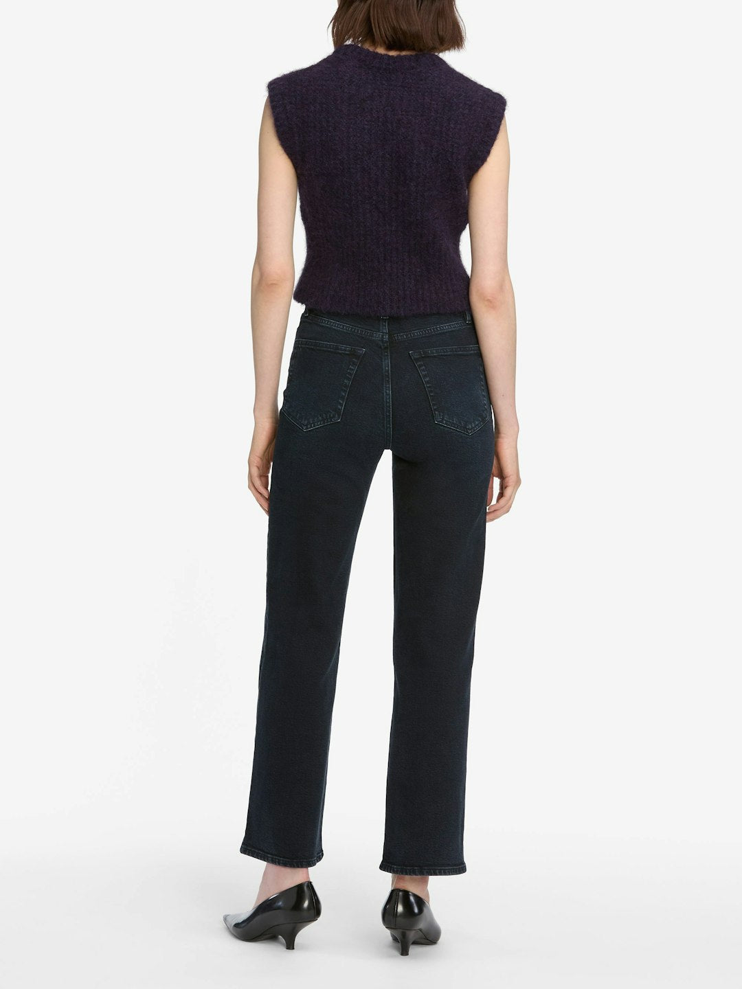 A person stands facing away, wearing a sleeveless dark purple top, Frame The Wide - Untold ultra high-rise wide leg jeans by Frame in a dark navy indigo wash, and black heeled shoes against a plain white background.